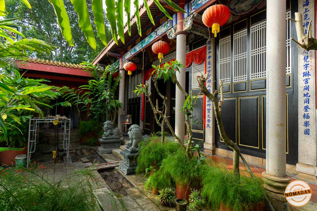 Patio exterior de un templo chino tradicional en Georgetown con farolillos rojos, columnas de piedra con caligrafía y estatuas de leones guardianes.