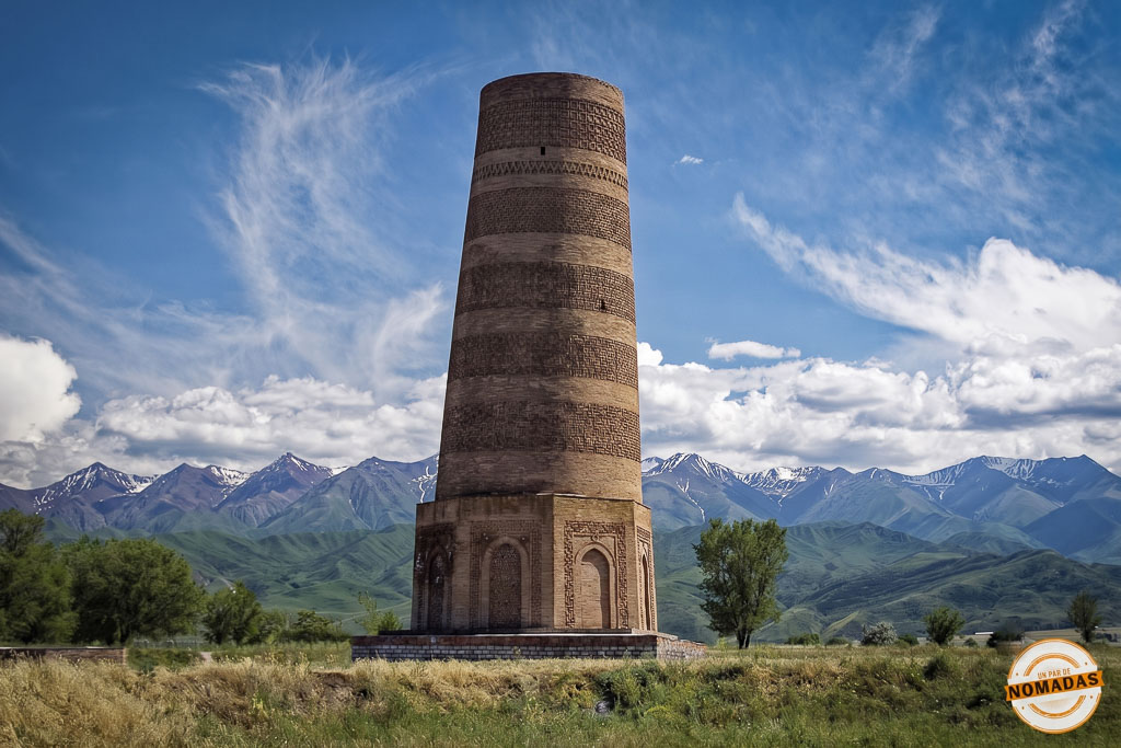 Antiguo e imponente minarete de ladrillo conocido como la Torre de Burana rodeado de un prado verde con montañas nevadas al fondo, una excursión histórica clave que ver cerca de Bishkek